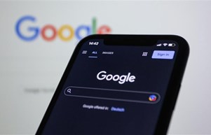 A smartphone displaying the google homepage, with a blurred google search bar as the background - symbolising googles new MUVERA algorithms